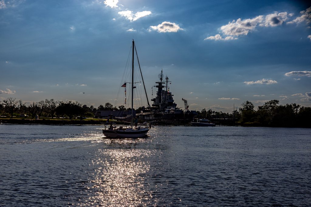 A sailboat travels north on the Cape Fear River in front of the battleship USS North Carolina.