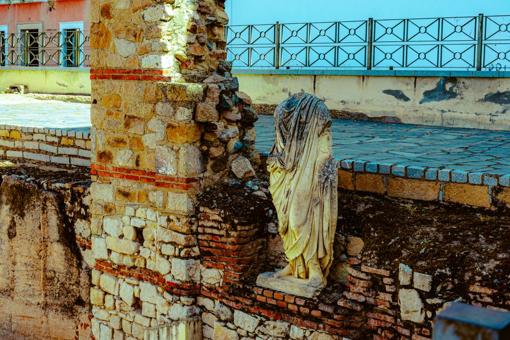 A headless statue stands on a ruined wall of the Pórtico del Foro Municipal de August Emérita.