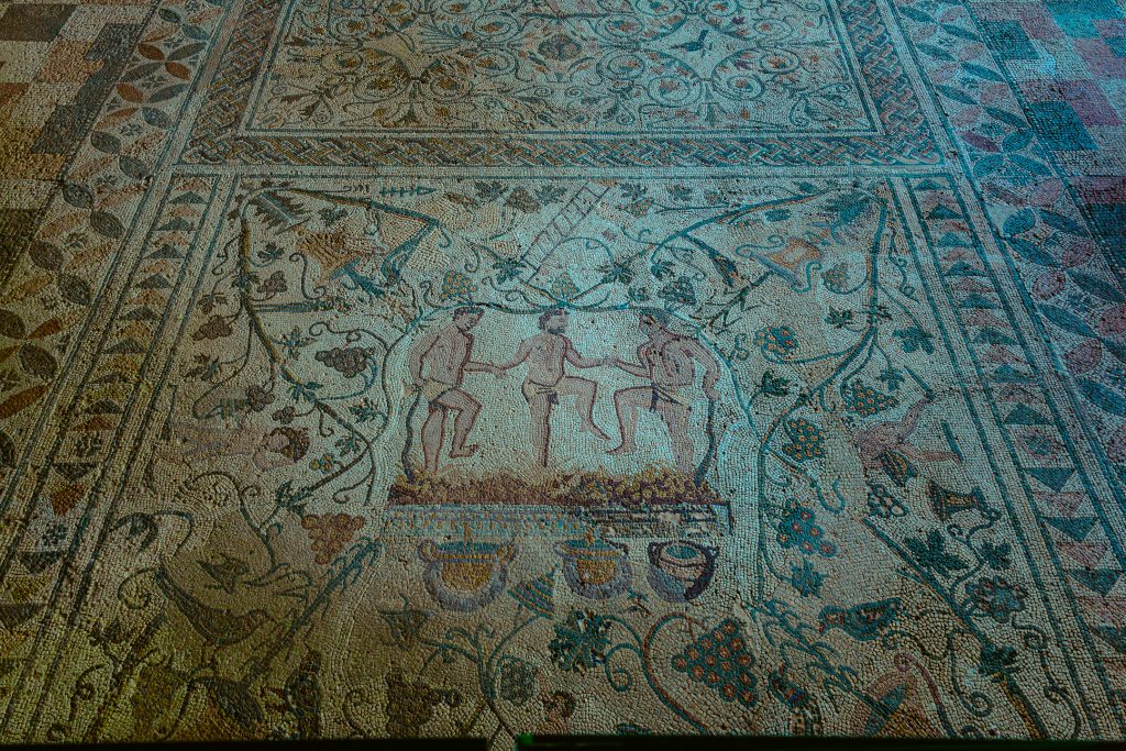 Ancient floor tiling depicts three men crushing grapes. Mérida, Spain.