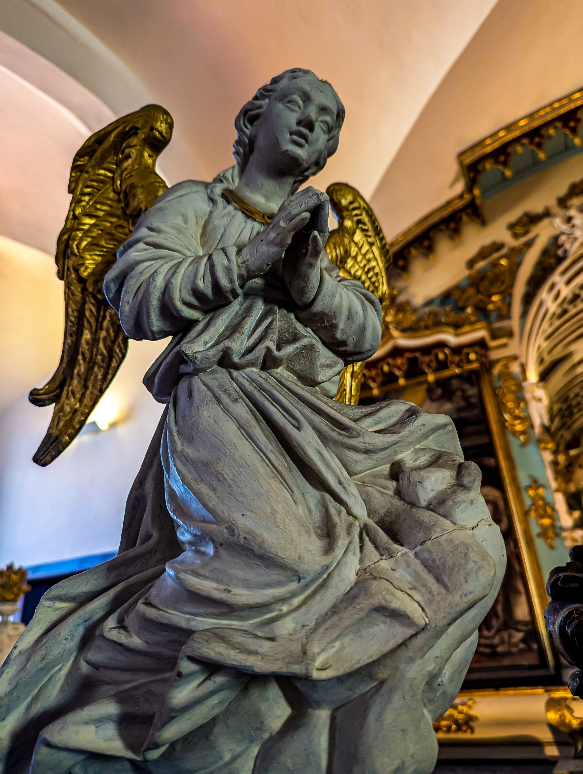 A statue of an angel holds it's hand together as if in prayer in the Capela dos Ossos, or Chapel of Bones in Évora, Portugal.